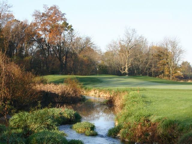 A golf course with a stream running through it and trees in the background.