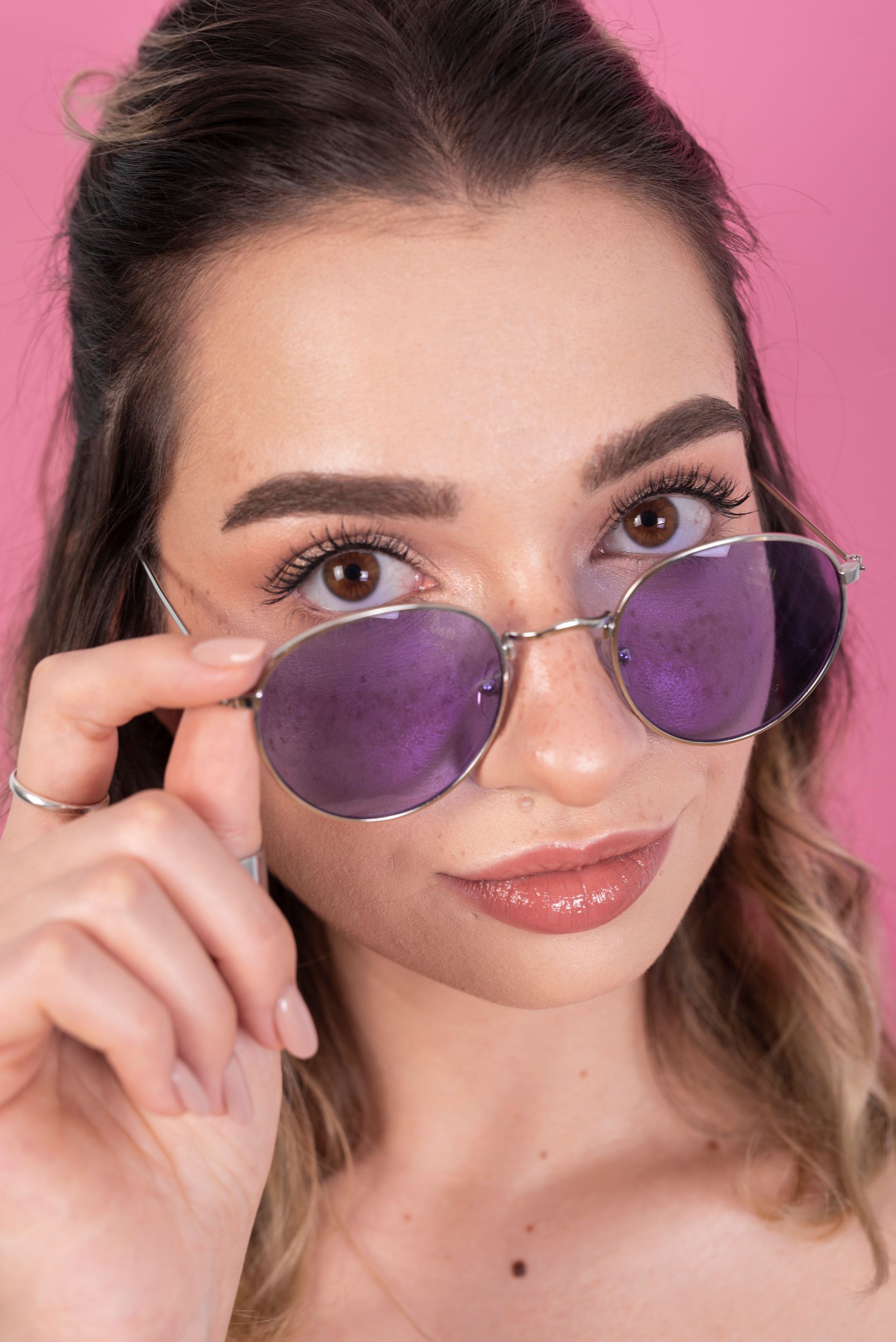 Una mujer que lleva gafas de sol de color morado sobre un fondo rosa.