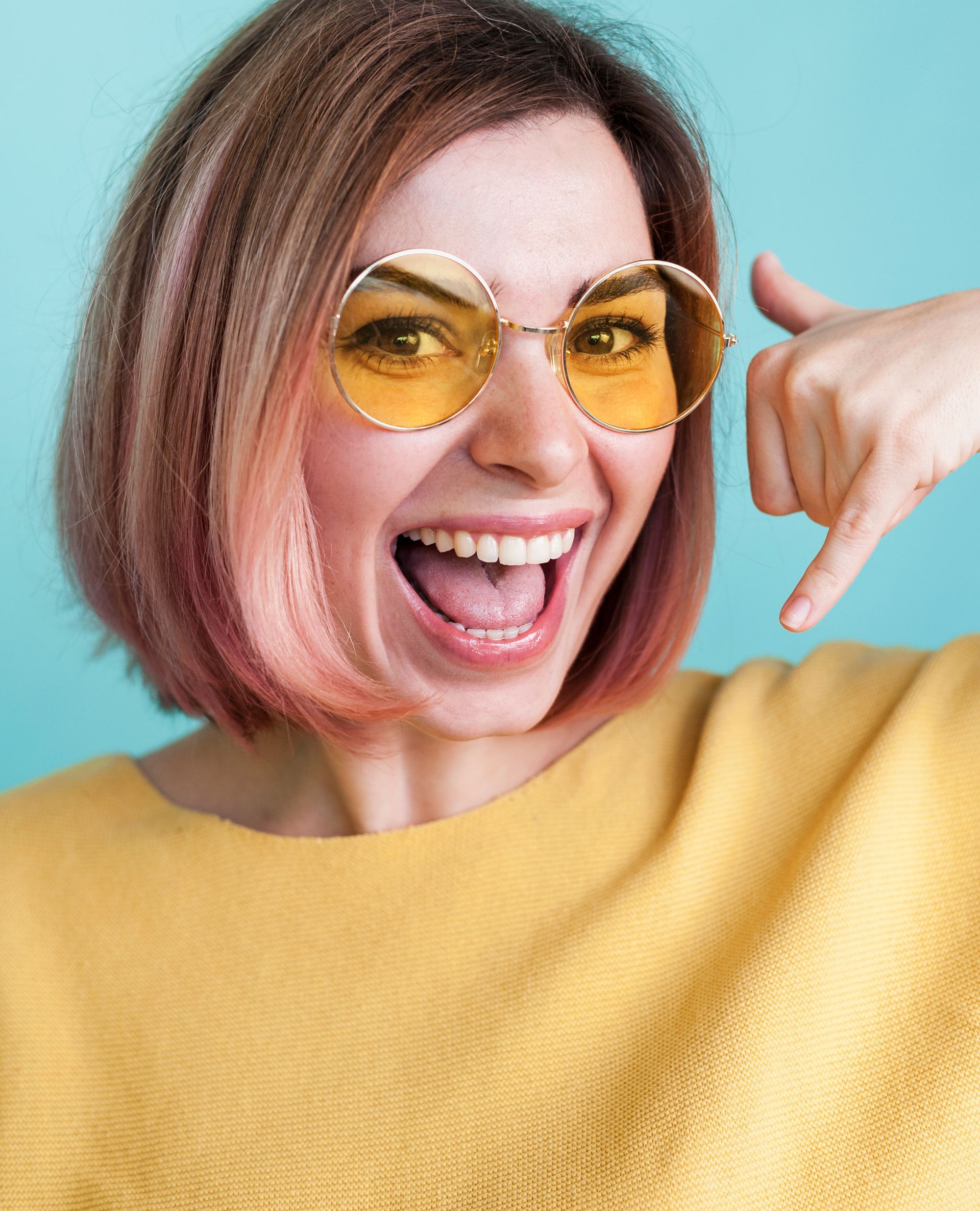 Una mujer que lleva gafas de sol amarillas y un suéter amarillo se señala a sí misma.