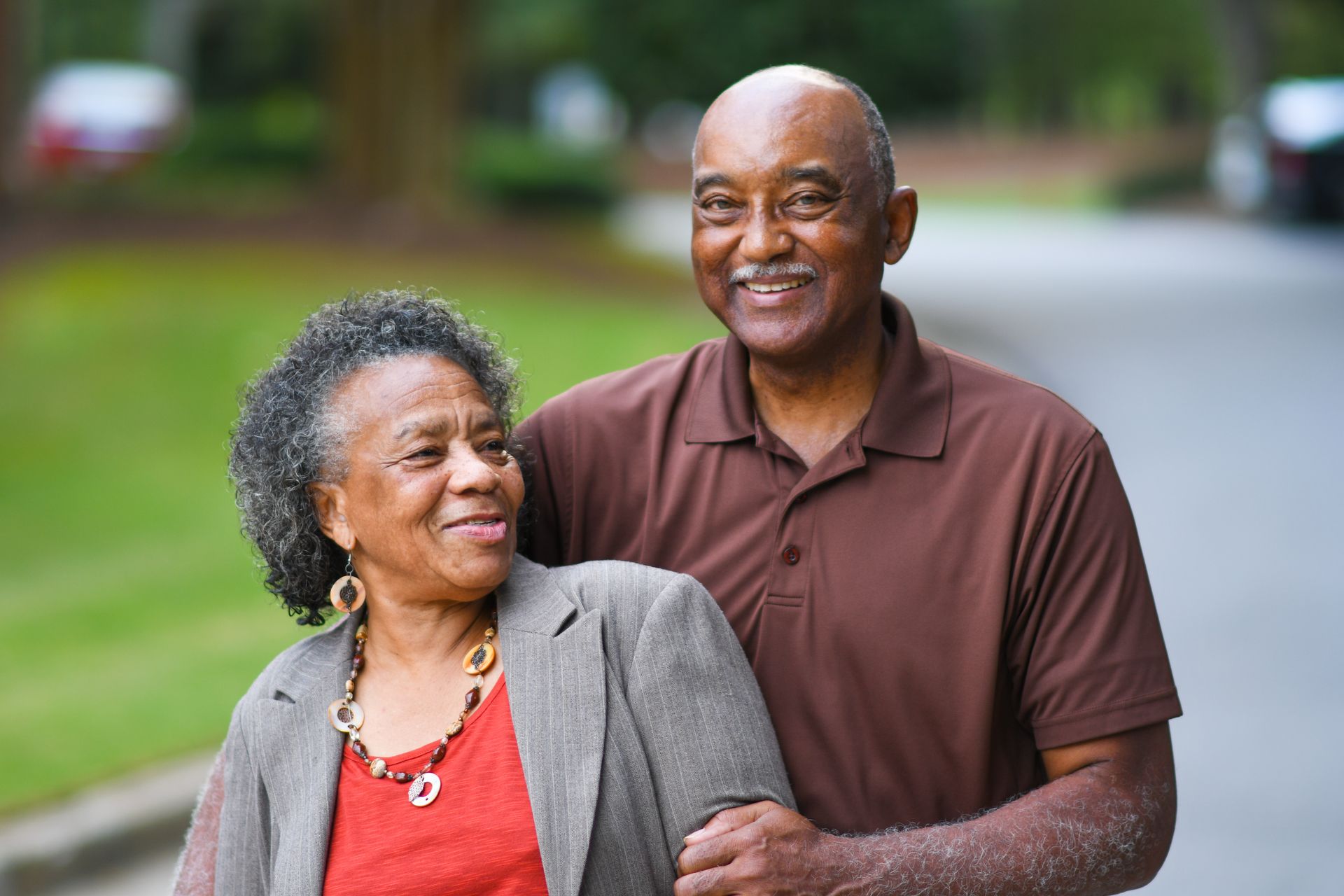 Smiling couple standing outdoors in a park, with trees and grass blurred in the background