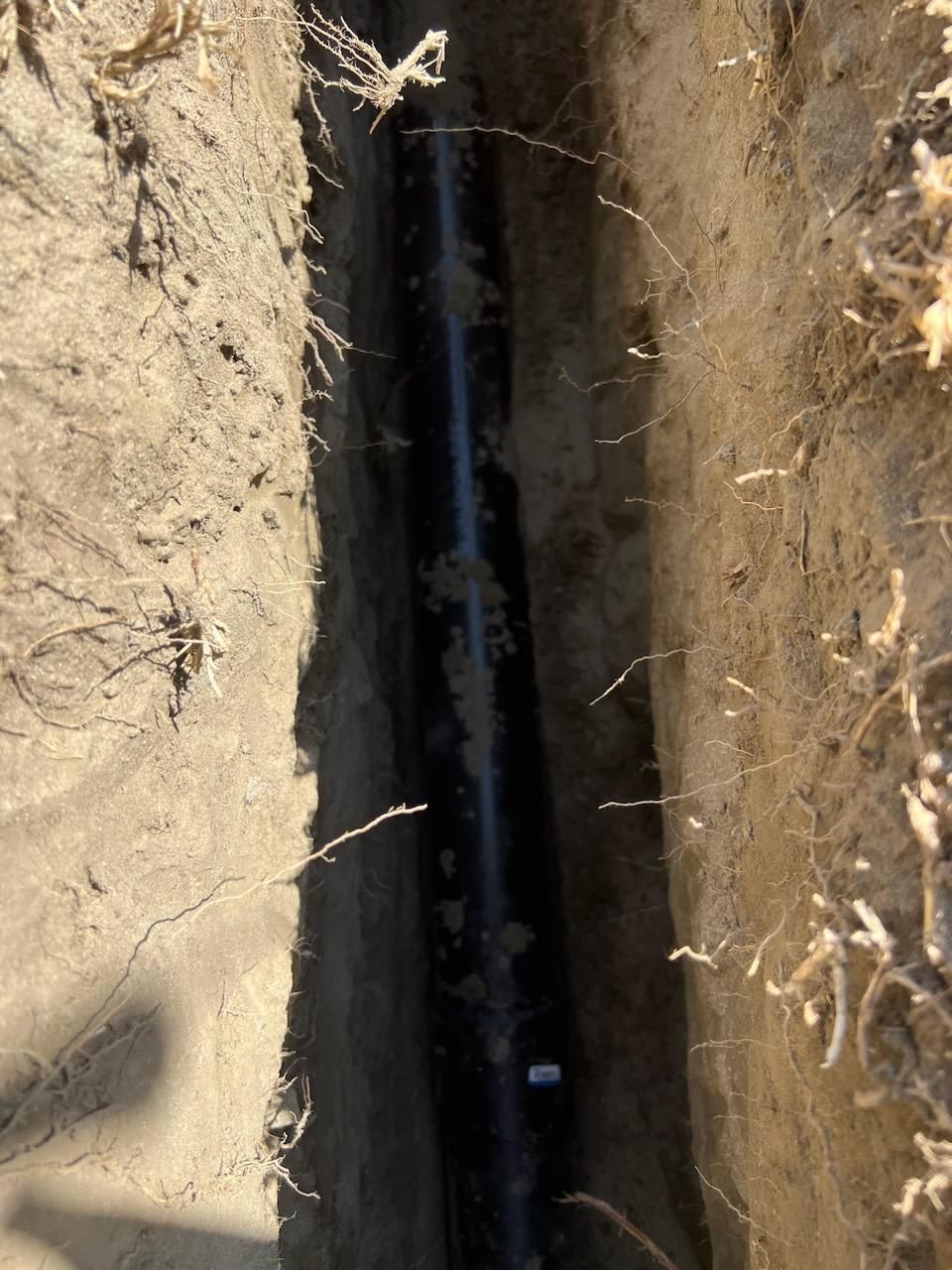A Black Pipe is Laying in the Dirt in a Trench