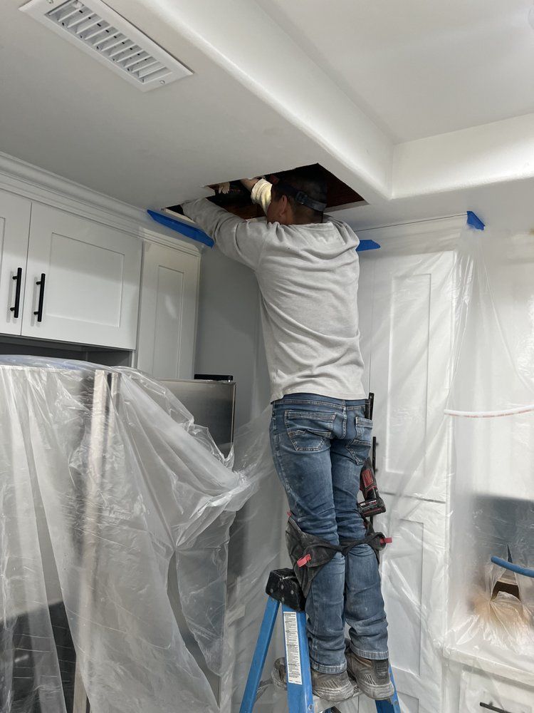 A Man is Standing on a Ladder in a Kitchen Looking Through a Hole in the Ceiling