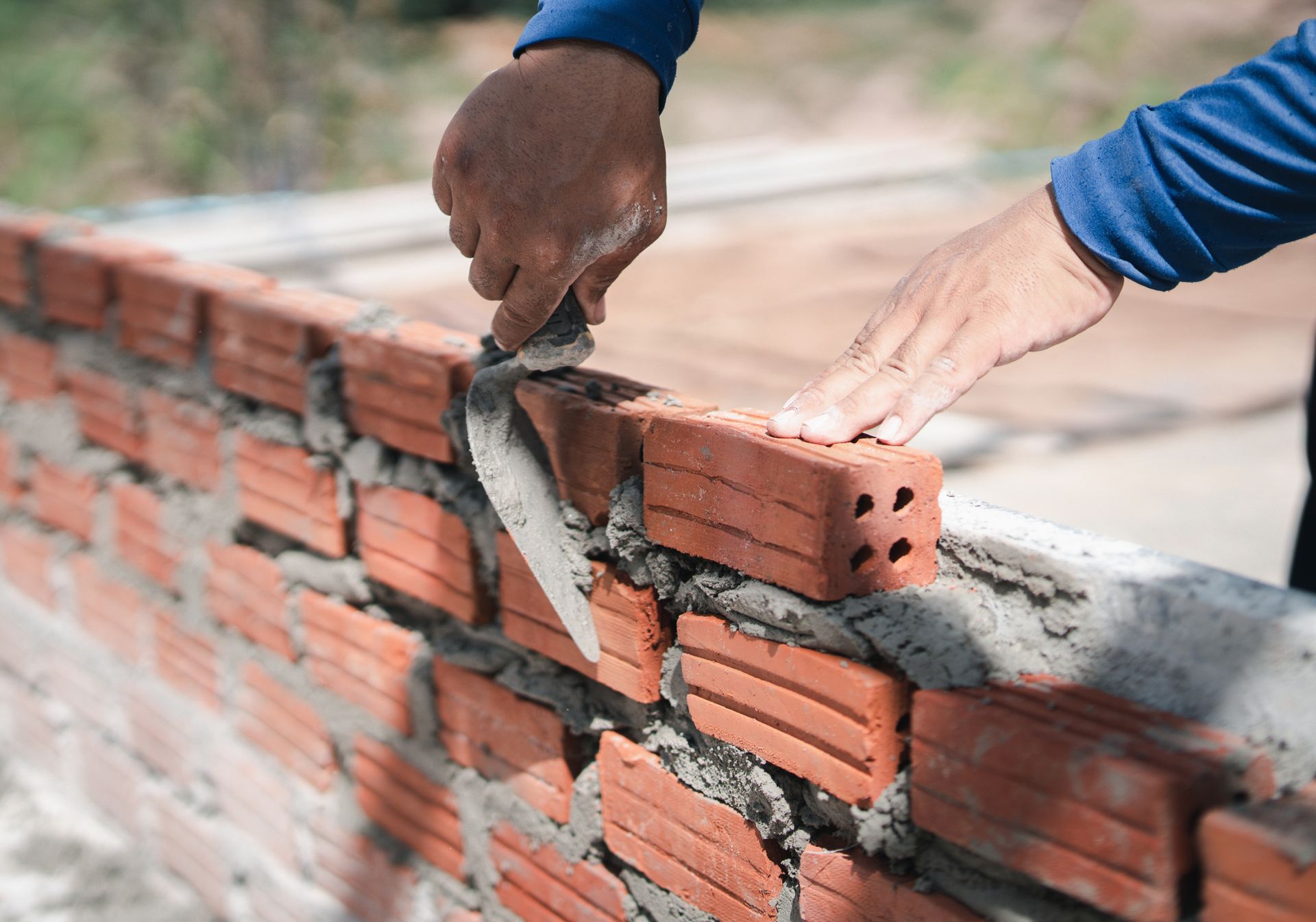 A man is laying bricks on a wall with a trowel.