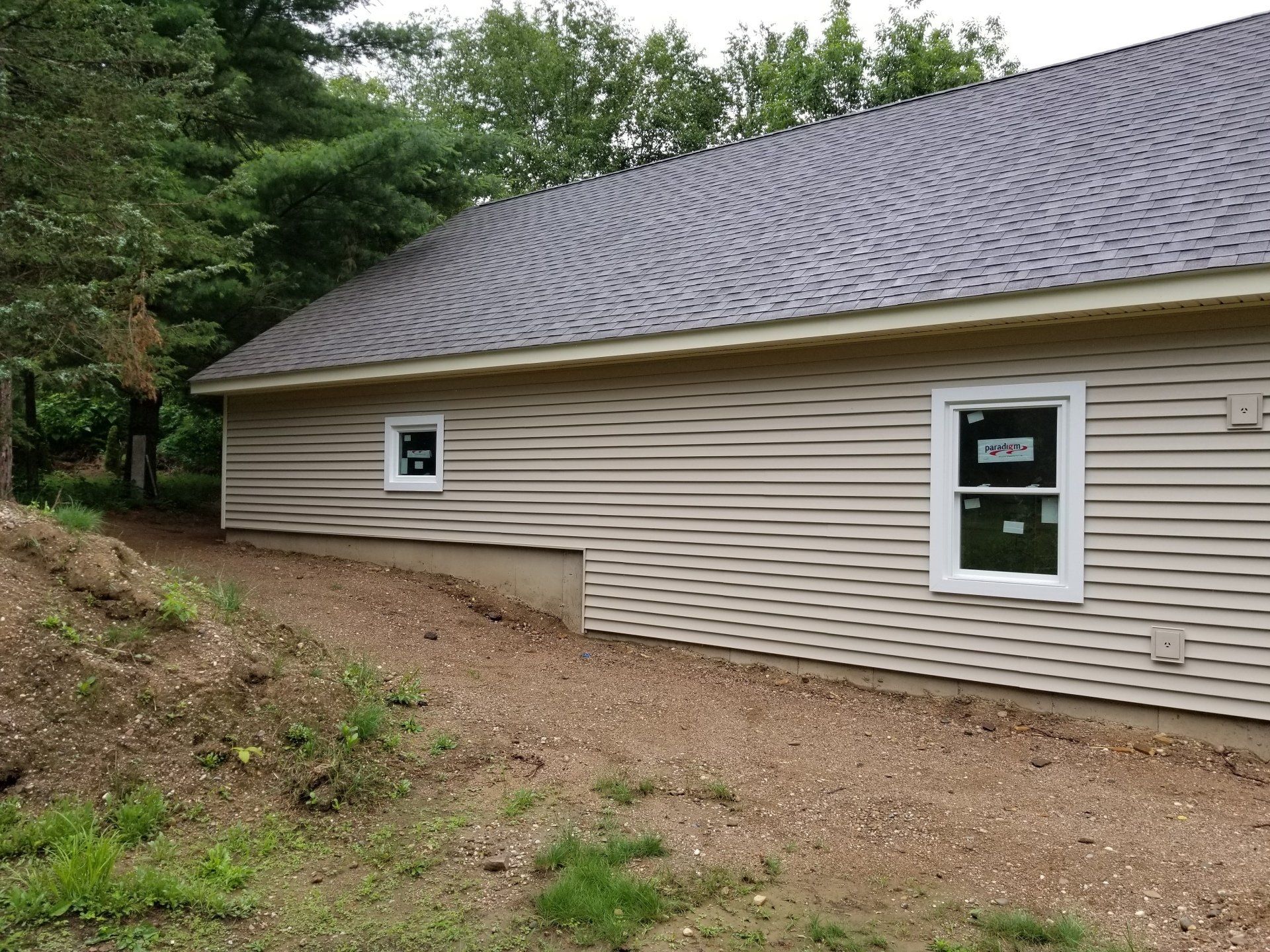 A newly constructed detached garage with light siding, an open double bay, and a framed window in the gable.