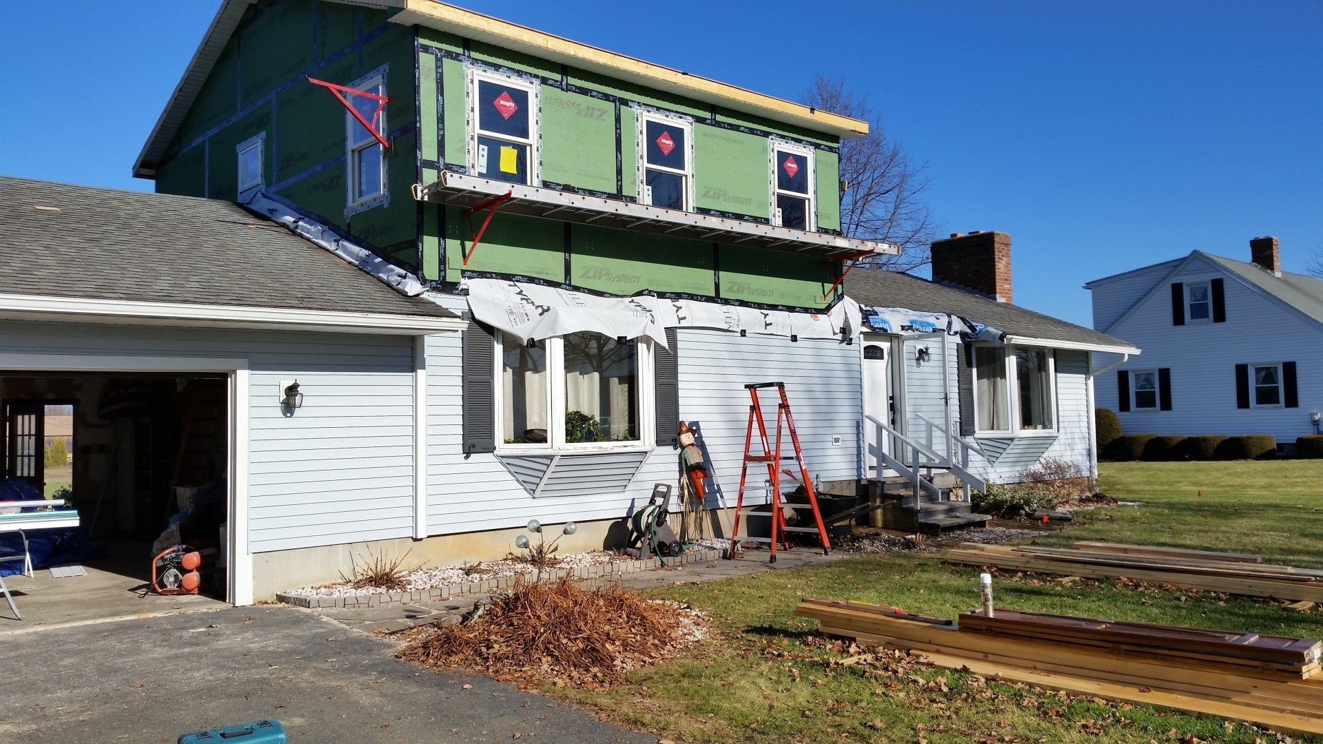 A two-story house undergoing renovation with exposed green sheathing on the top floor and white siding on the bottom.