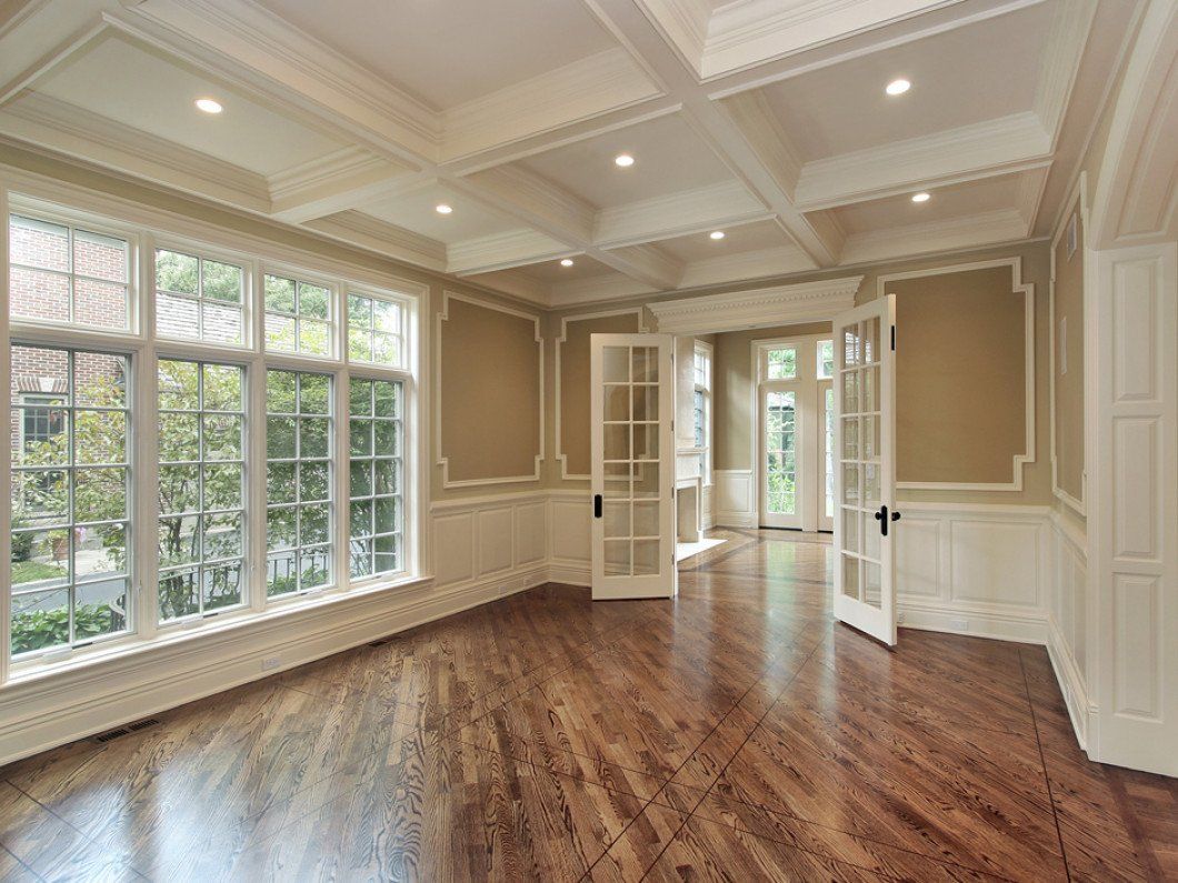 A bright, white kitchen with a large marble island, two wooden chairs, and a hanging pot rack above a wood floor.