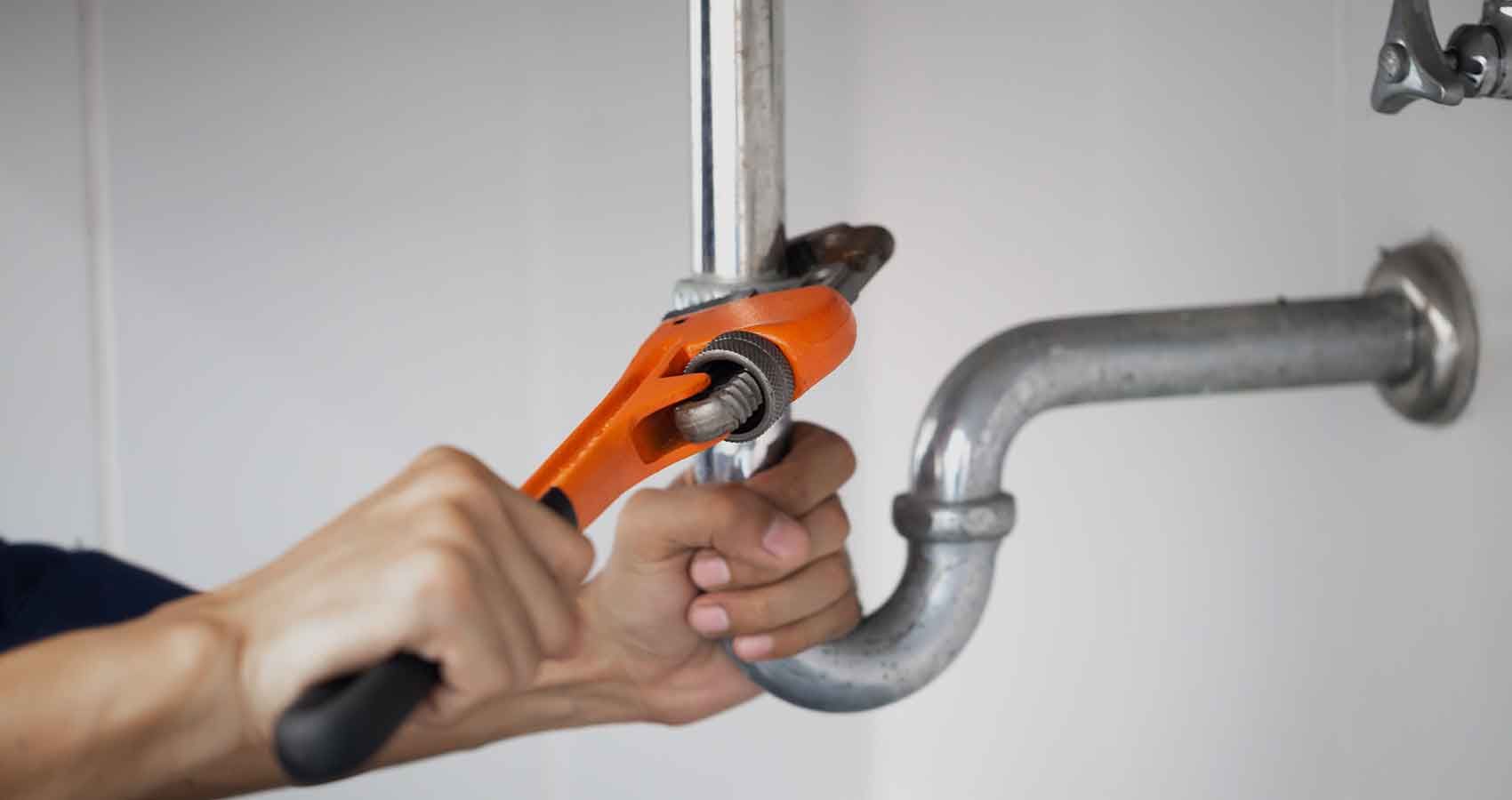 A plumber is fixing a pipe with a wrench.