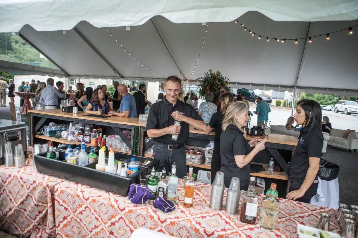A group of people are standing around a bar under a tent.