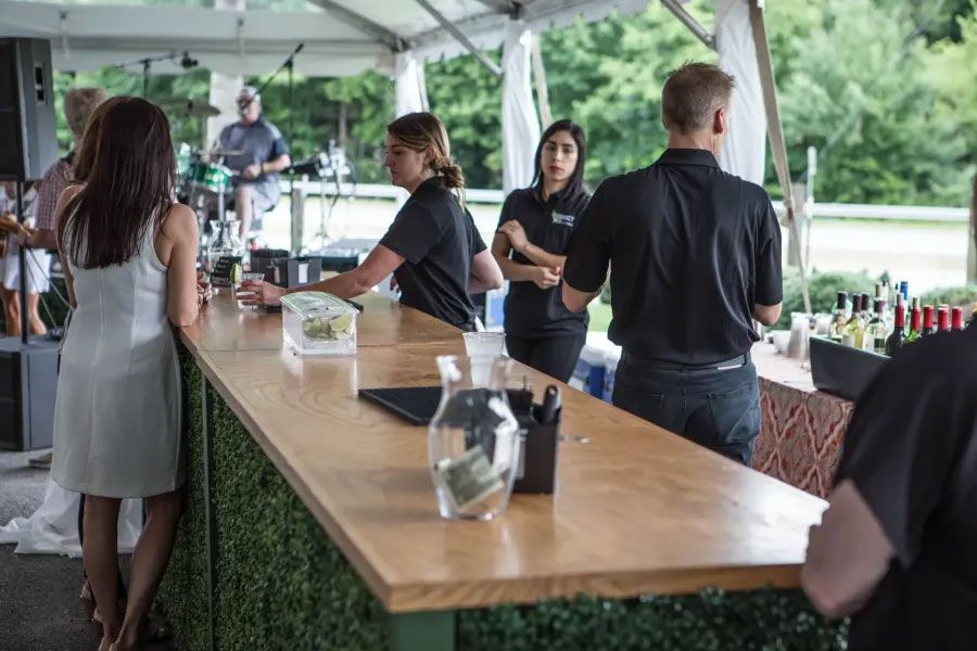 A group of people are standing around a long wooden bar.