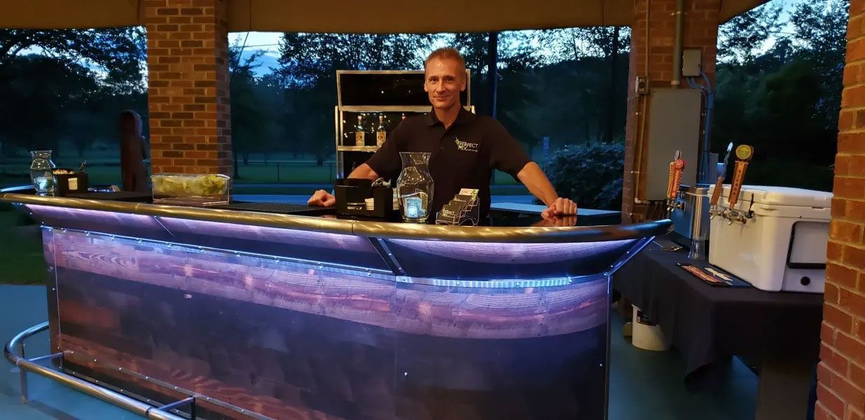 A man is standing behind a bar with purple lights on it.