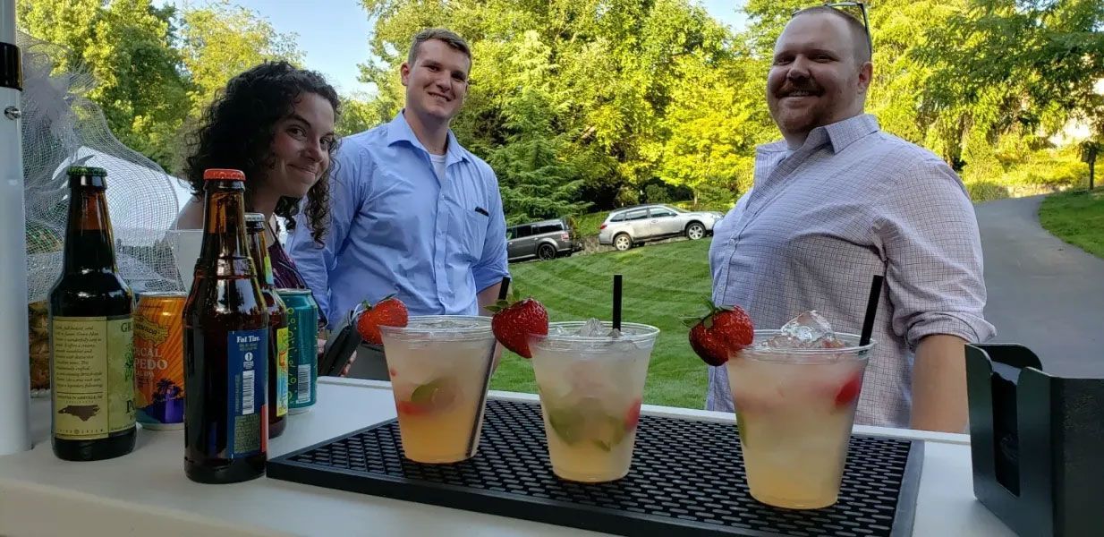 A group of people are standing around a table with drinks on it.