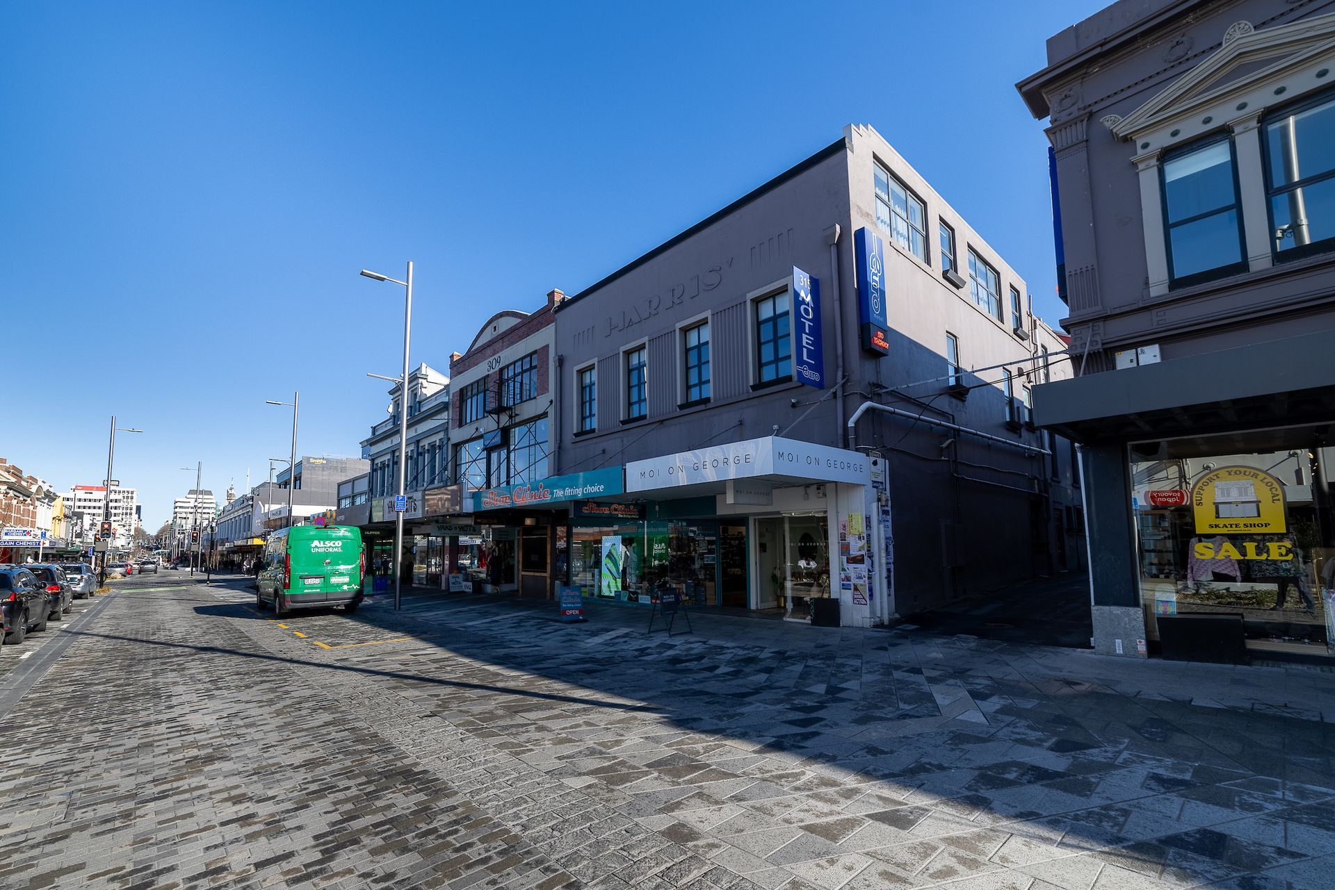 A green bus is driving down a city street next to a large building.