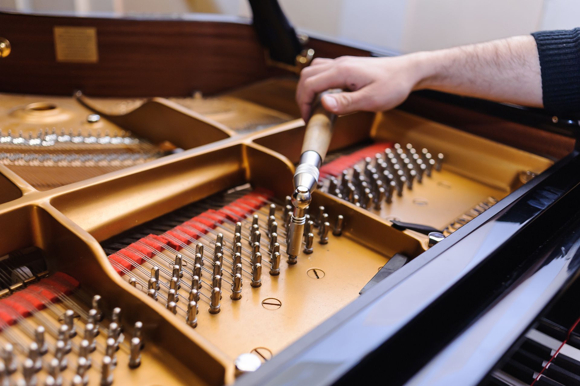 A person is working on a piano with a tuning tool.