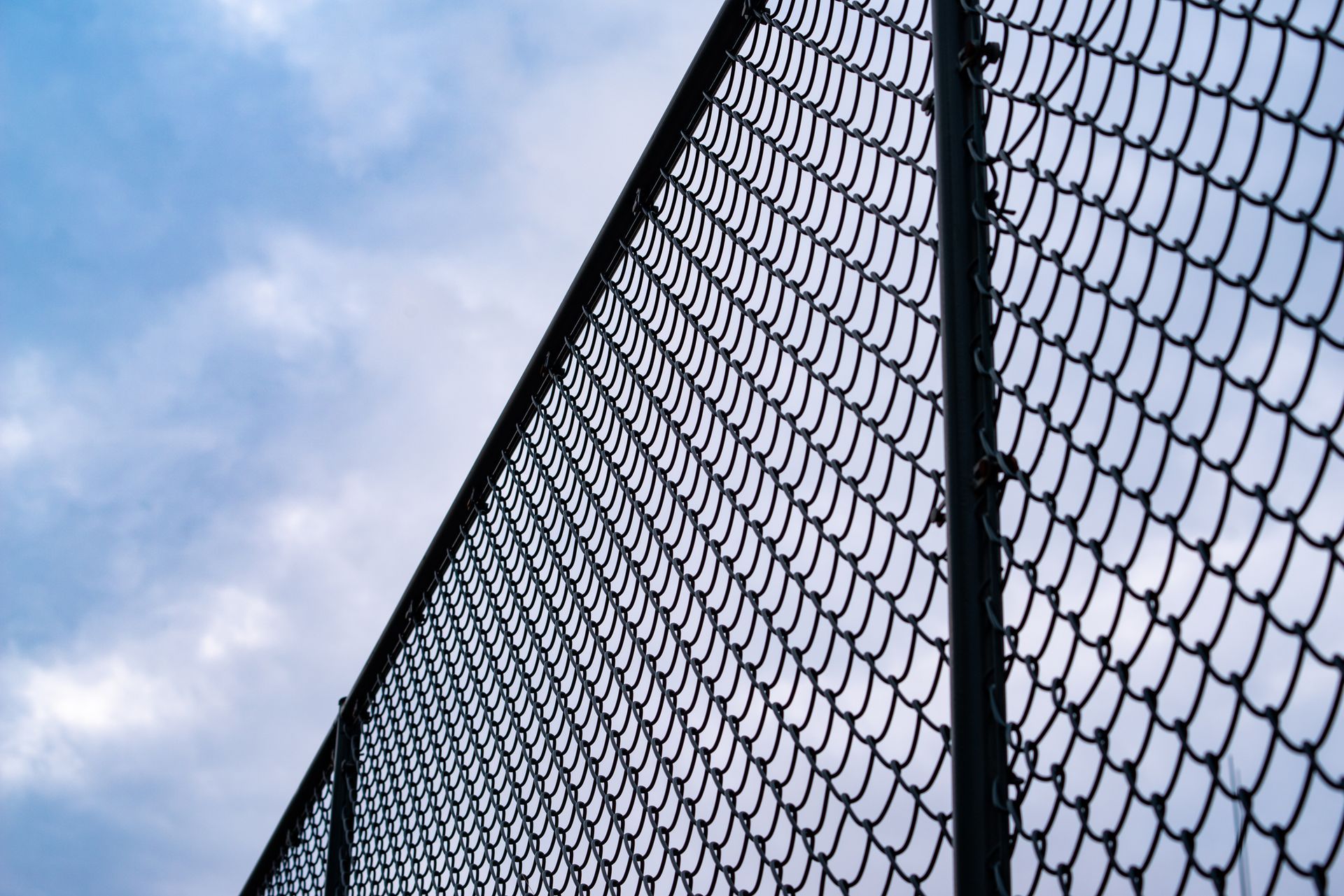 A chain-link fence stretches diagonally across the frame against a blue sky with scattered white clouds.