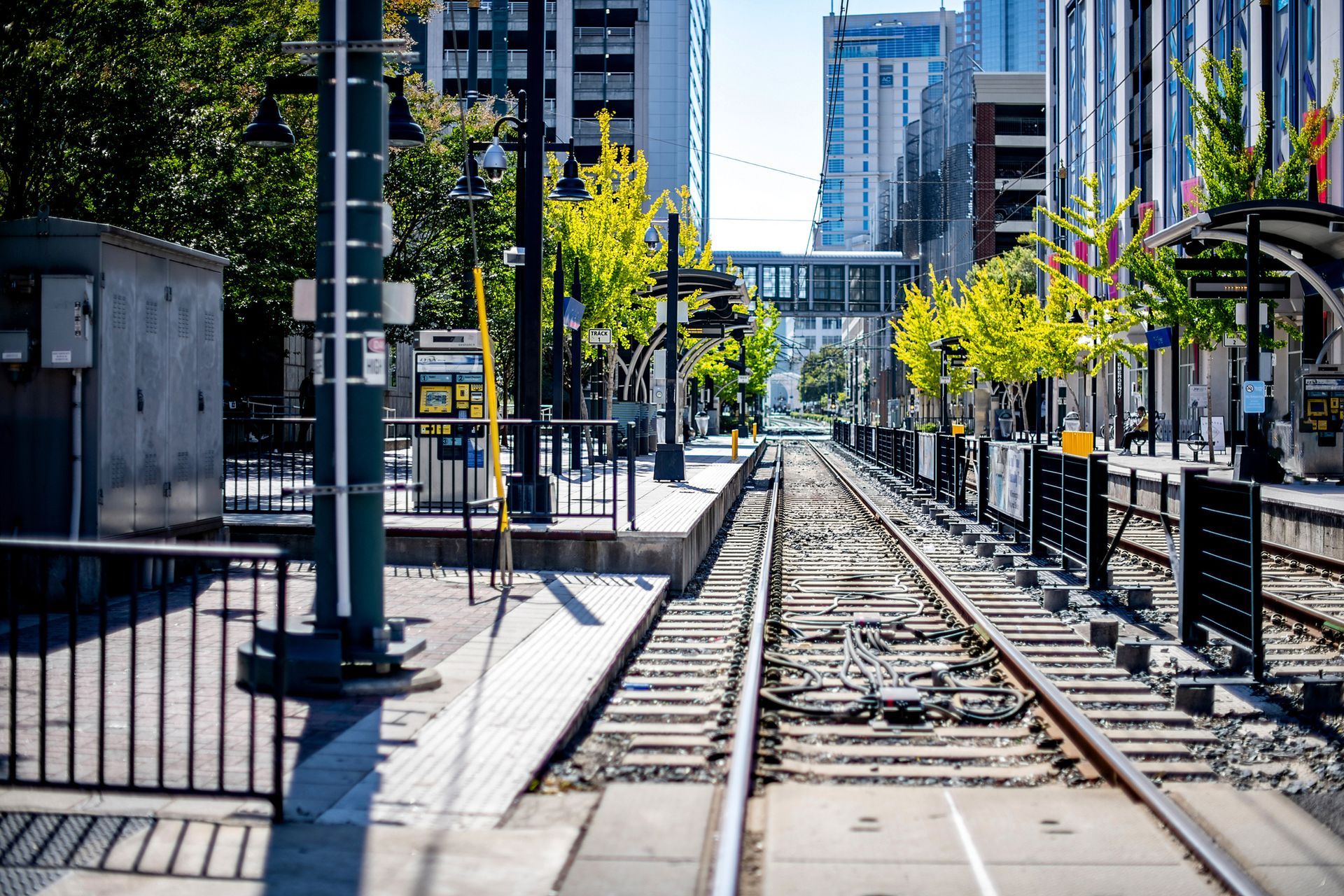 A low-angle view of empty light rail tracks running between modern city station platforms under bright daylight.