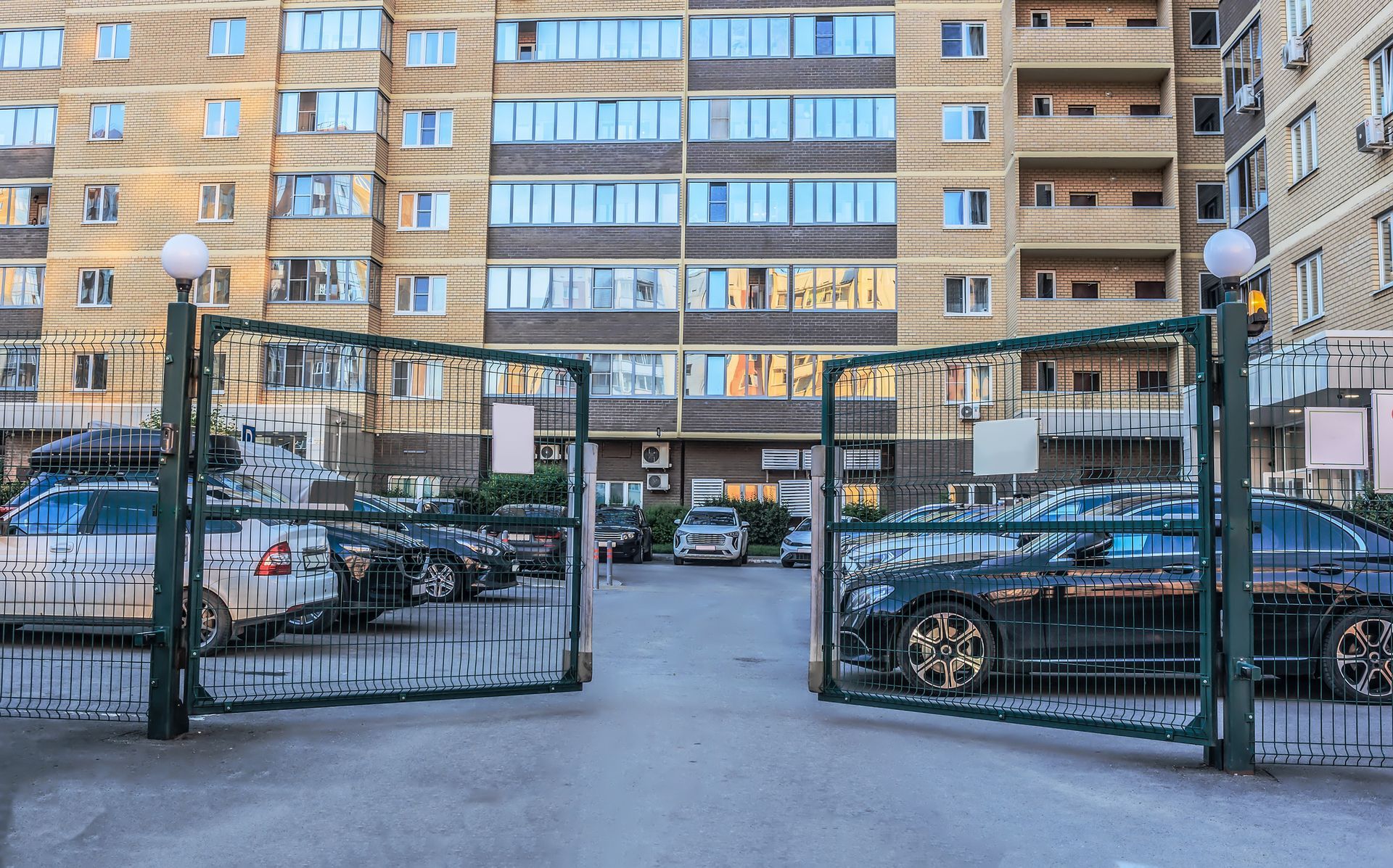 Open gates to a parking area in front of a multi-story, beige apartment building.