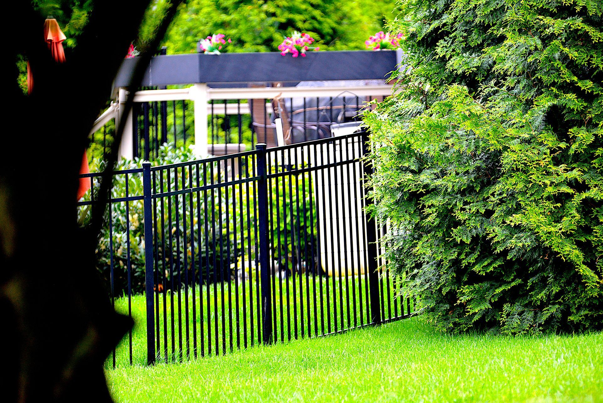 A black metal fence sits on a green lawn with trees and a deck structure in the background.