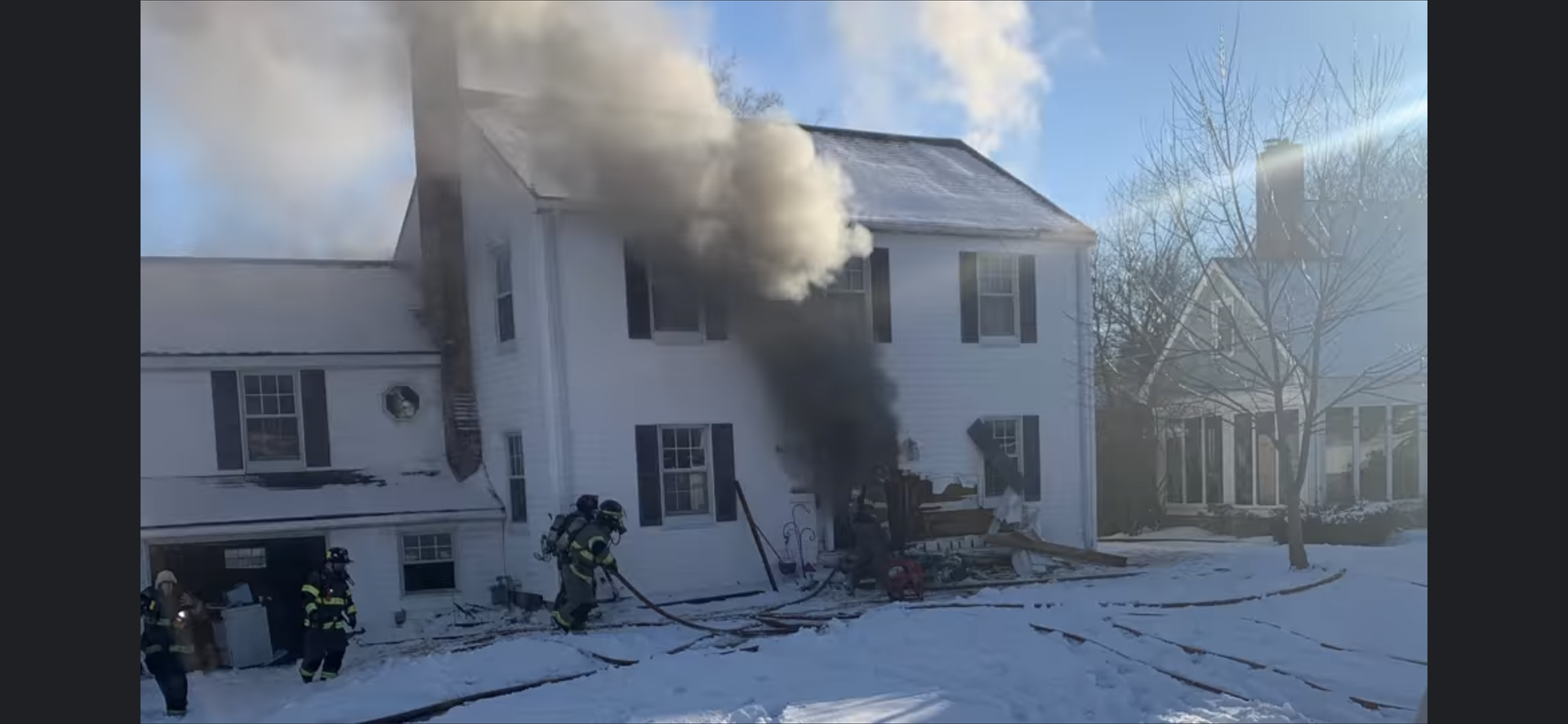 Smoke is coming out of a home that is on fire with firefighters working.