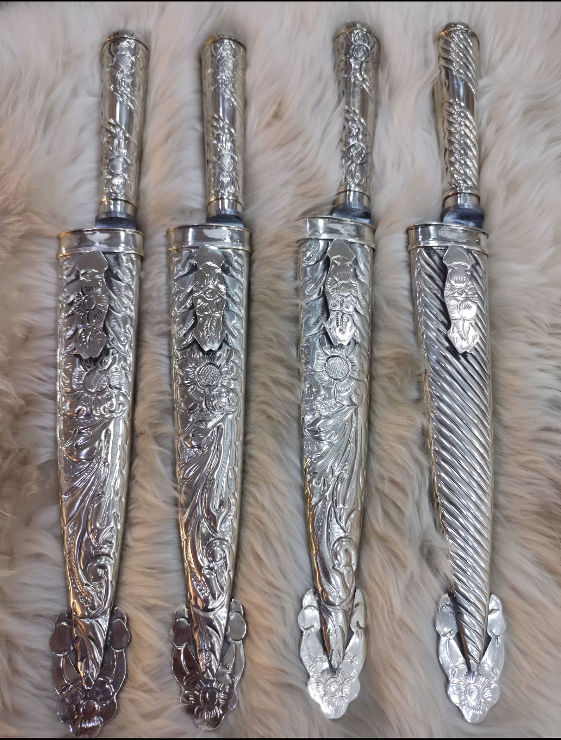 Cuatro cuchillos de plata ornamentados en fundas decorativas, exhibidos sobre una superficie peluda.