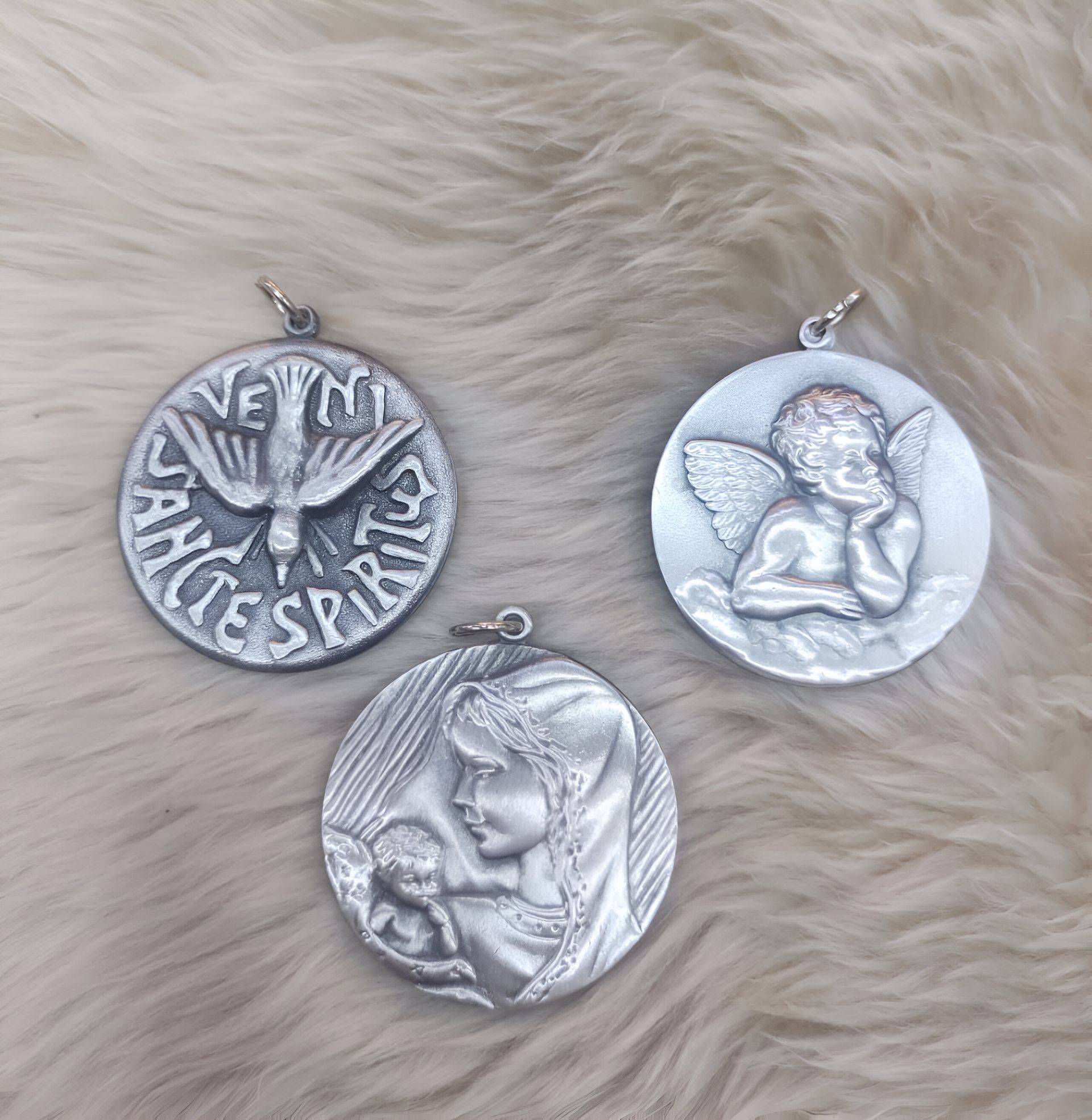 Tres colgantes religiosos de plata: paloma, ángel y Virgen con el niño.