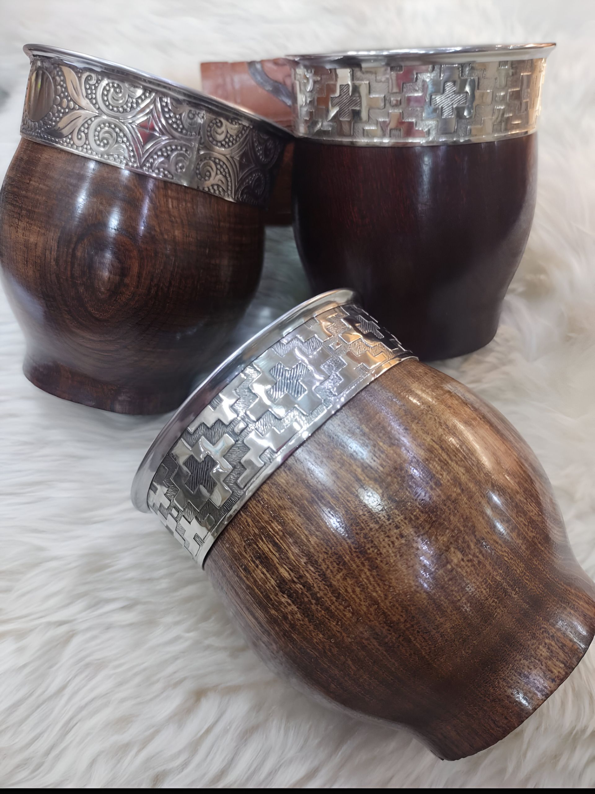 Tres mates de madera oscura con bordes plateados, sobre una superficie blanca esponjosa.