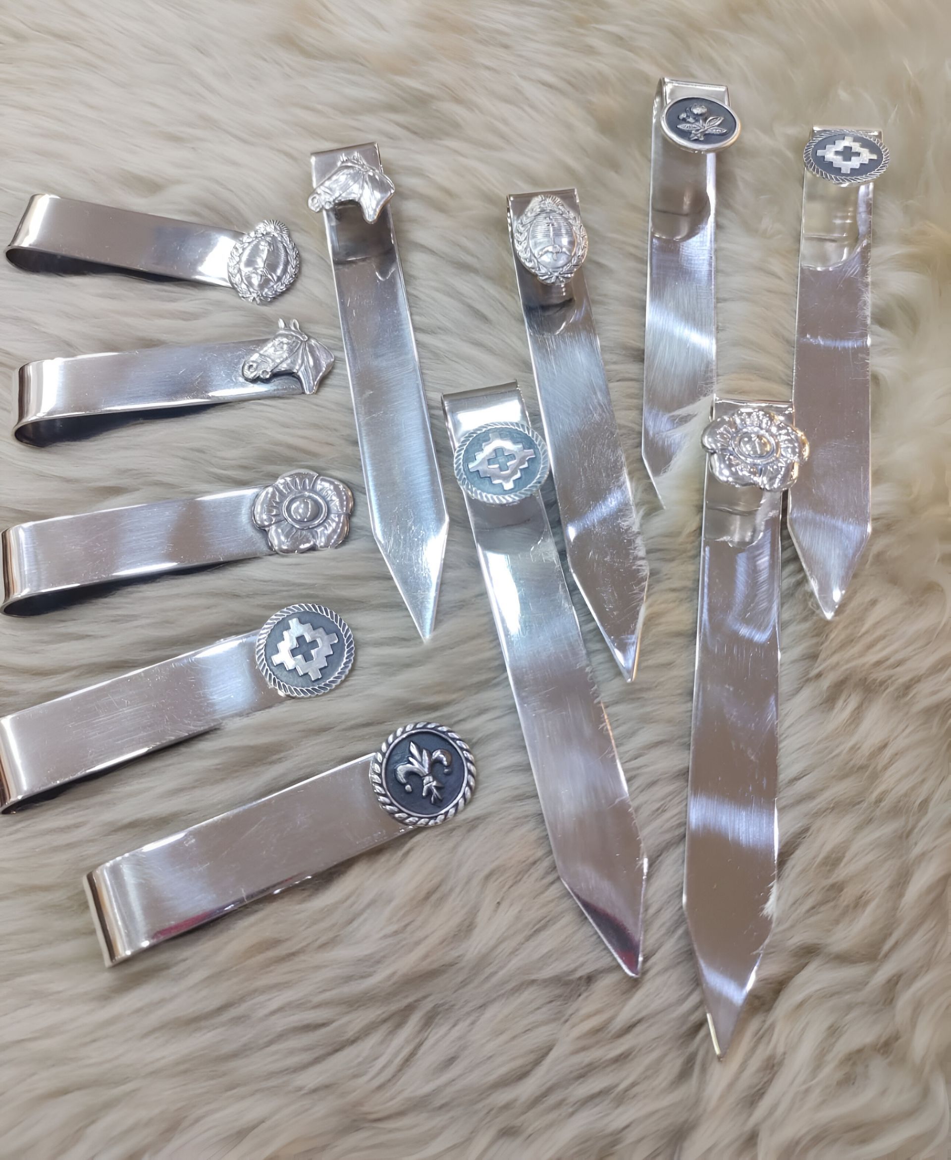 Marcadores de metal plateado con adornos decorativos, dispuestos sobre una superficie difusa de color marrón claro.