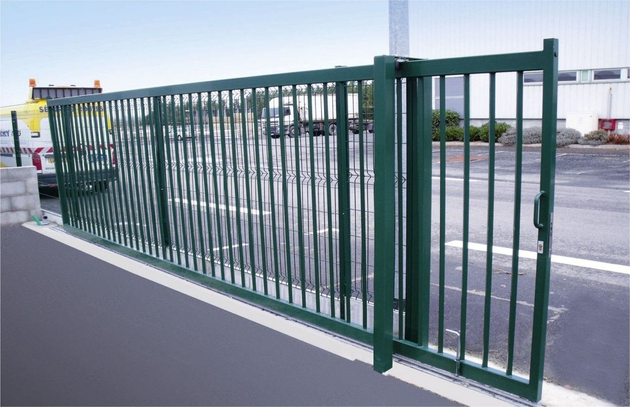 A green fence is surrounding a parking lot.