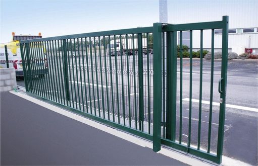 A green fence is surrounding a parking lot.