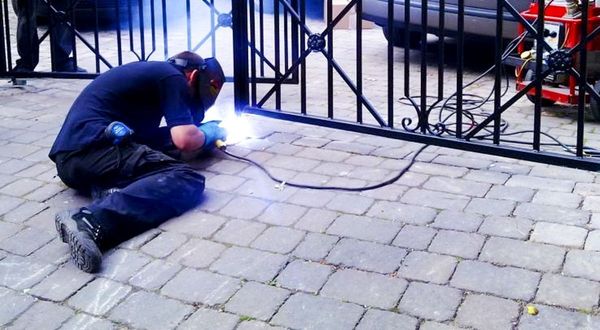 A man is kneeling on the ground welding a gate