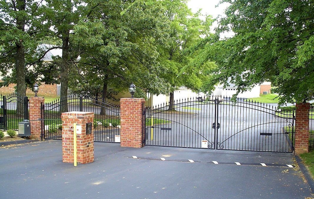 A large gate with brick pillars is surrounded by trees.