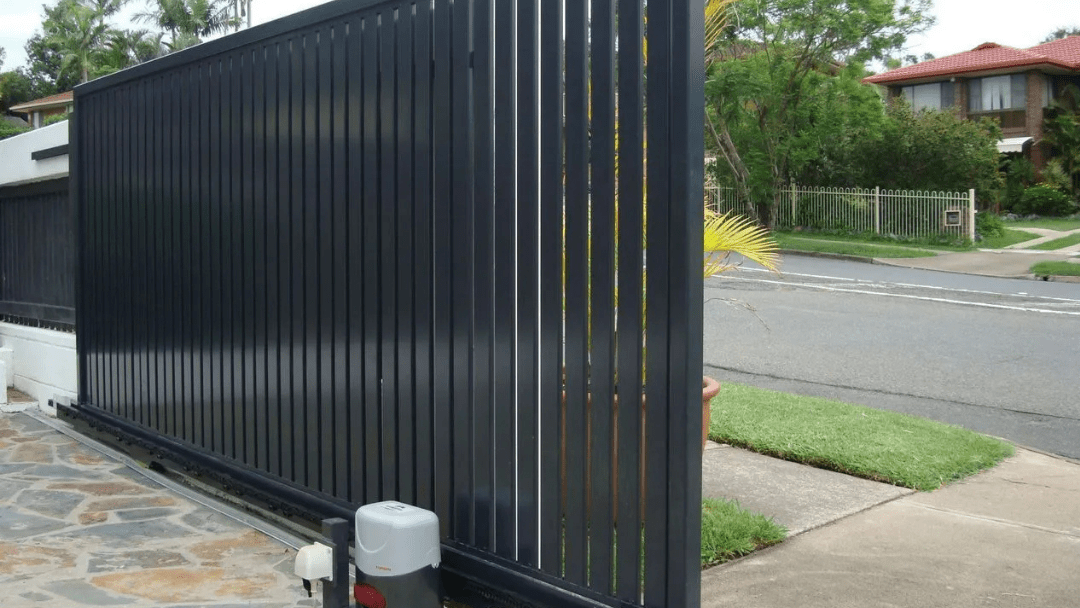 Black slatted driveway gate beside a suburban street and sidewalk