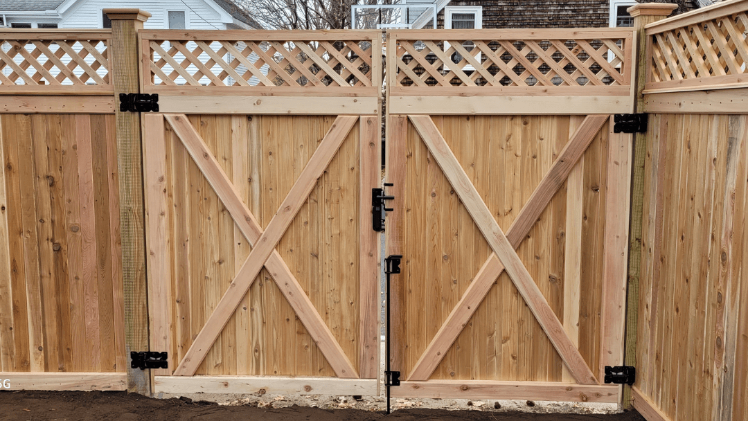 Wooden double gate with diagonal cross braces and black hinges in a fenced yard