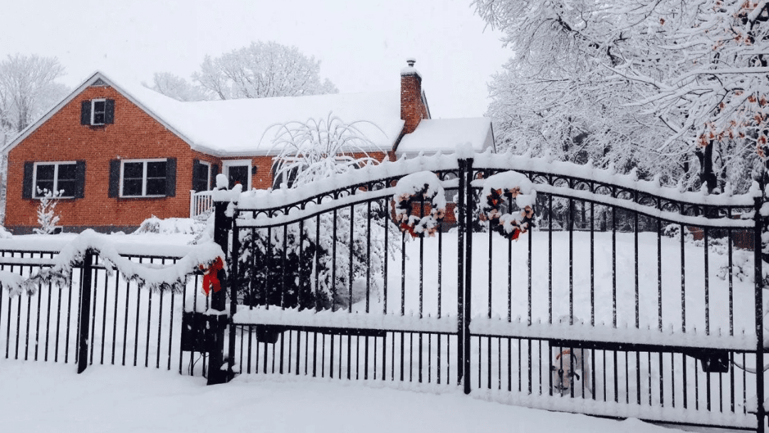 Snow-covered house behind a black wrought-iron gate in winter