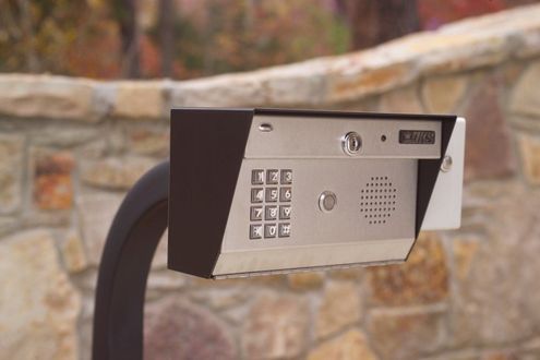 A keypad on a pole with a stone wall in the background