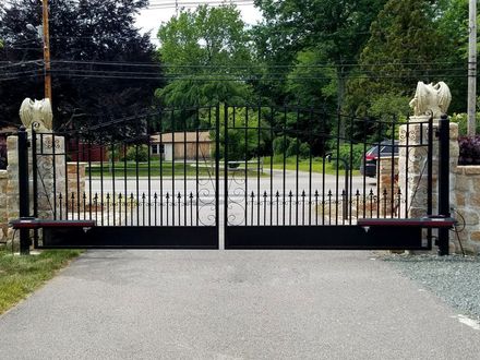 A black wrought iron gate is open to a gravel driveway