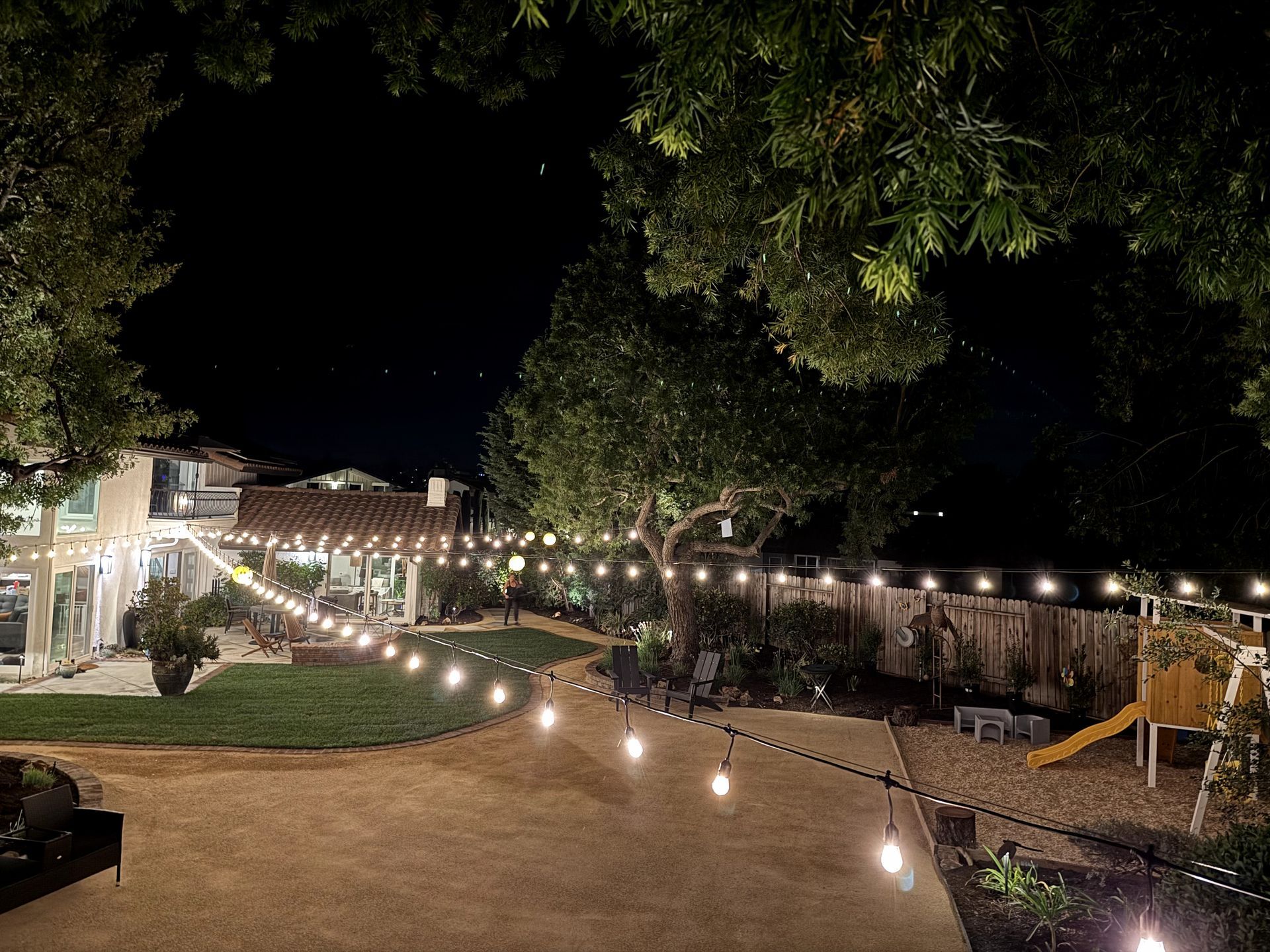 A backyard with a playground and string lights at night.