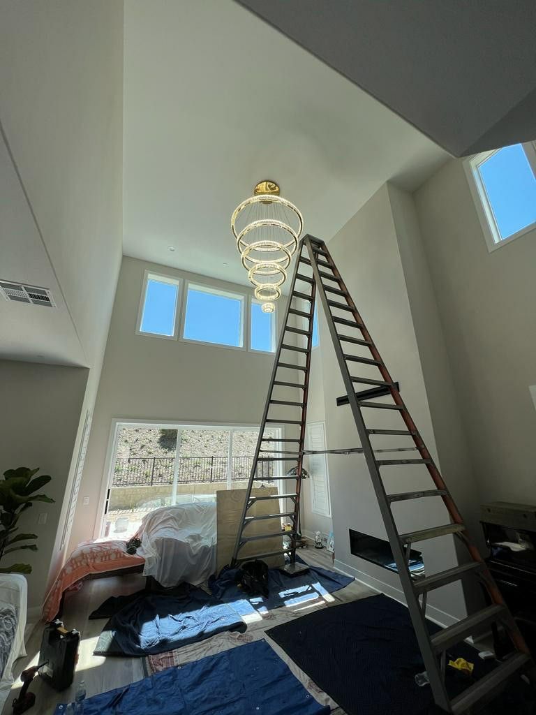 A ladder is sitting in a living room next to a chandelier.