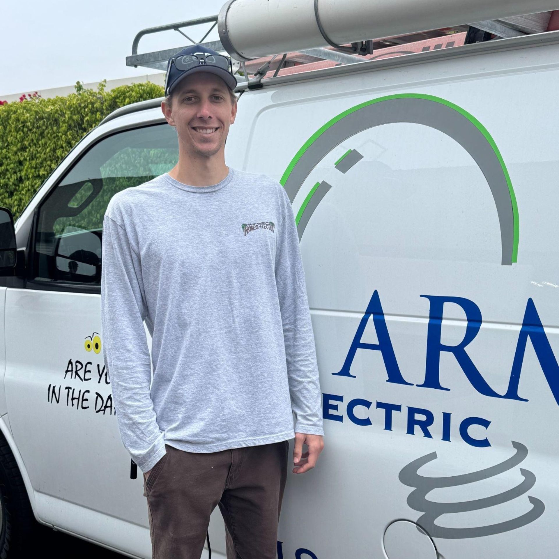 Smiling man standing by a white ARAM electric service van with logo and roof equipment