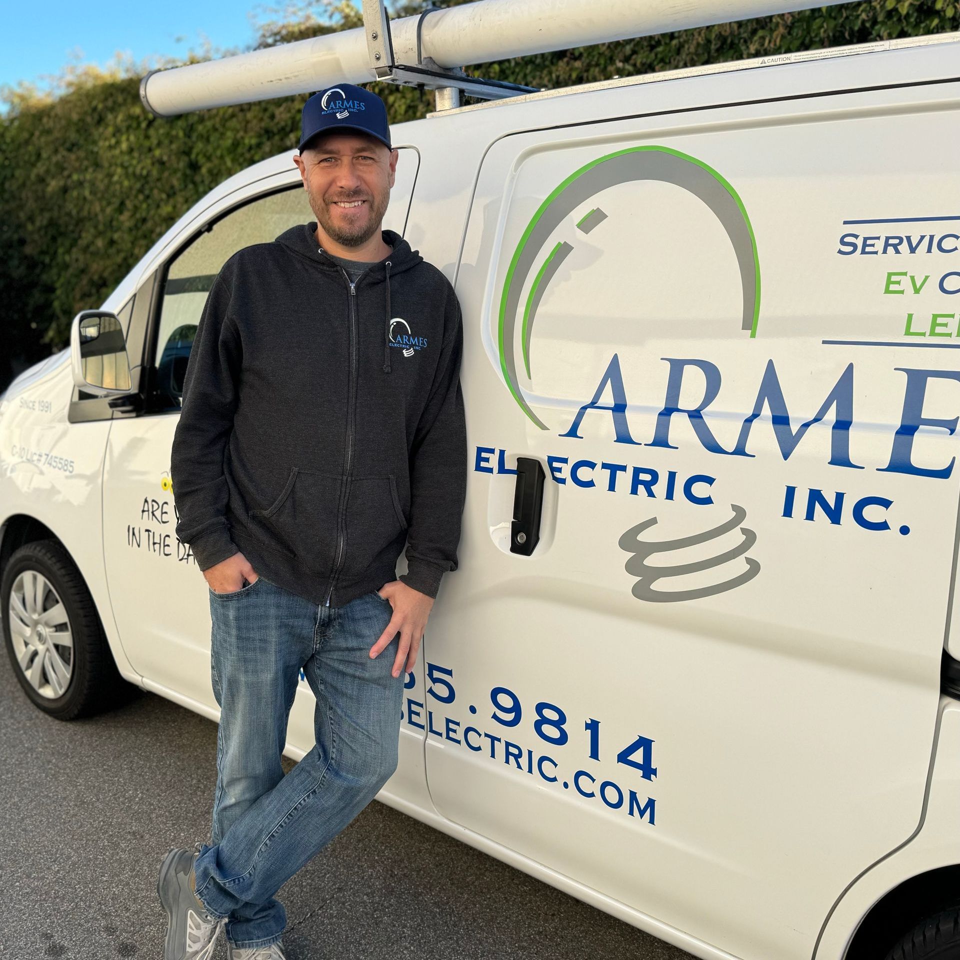 Man standing beside a white armored electric service van with company logo and roof-mounted ladder
