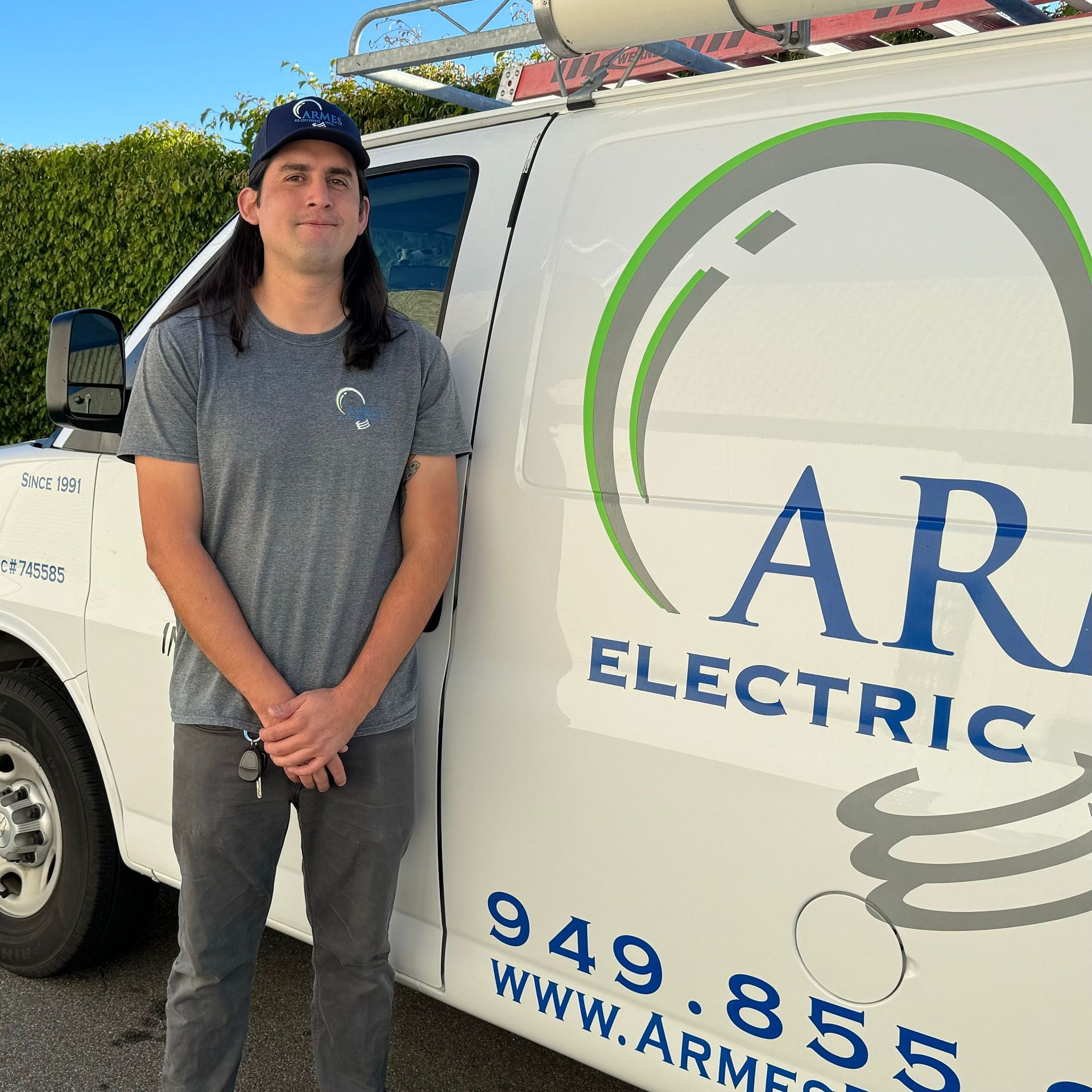 Person standing beside a white AR Electric service van with company logo and phone number.