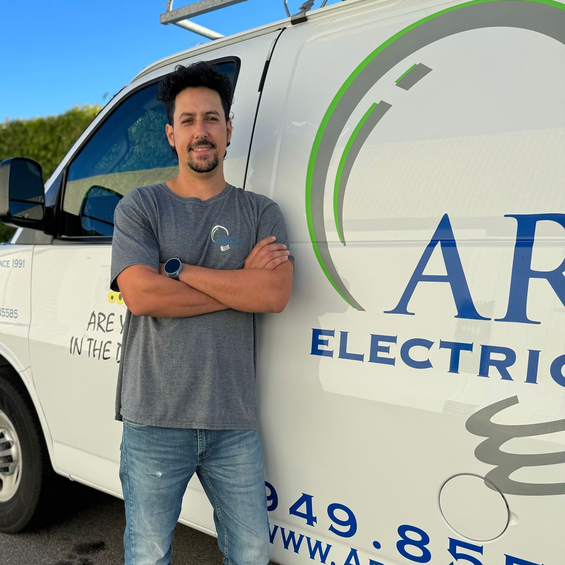 Man standing with arms crossed beside a white electric service van with company logo