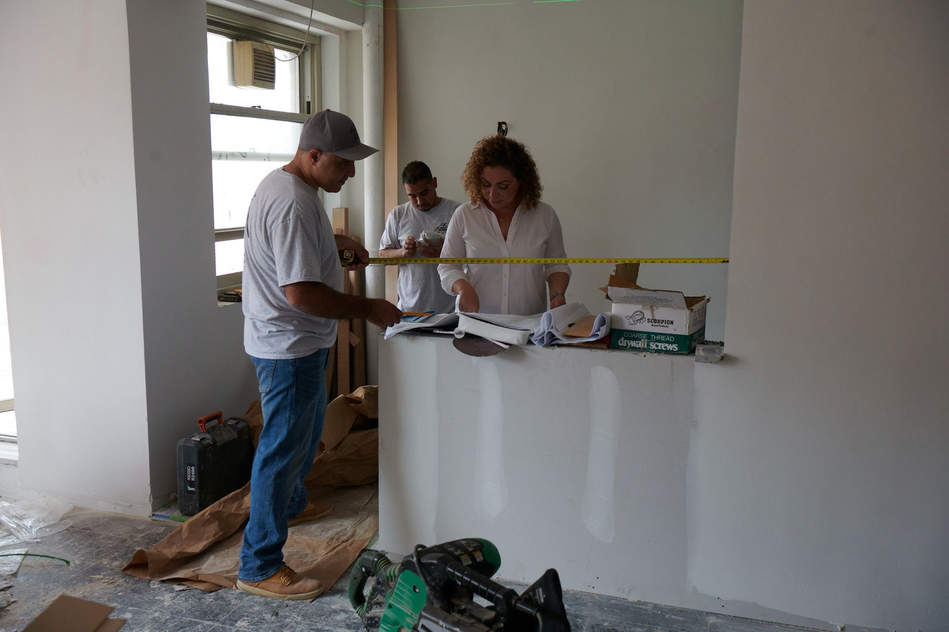 A man and a woman are measuring a wall with a tape measure.