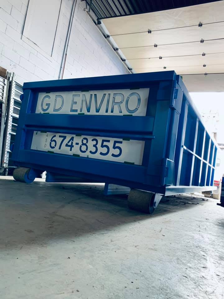 Blue G&D Enviro dumpster in a warehouse, with the number 674-8355 displayed on the back.