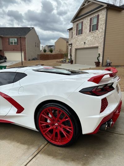 A white sports car with red wheels is parked in front of a house