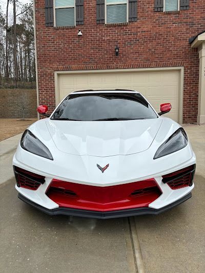 A white corvette with red trim is parked in front of a brick house.