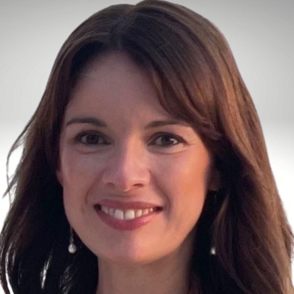 Headshot of a smiling person with shoulder-length brown hair against a plain, light gray background.