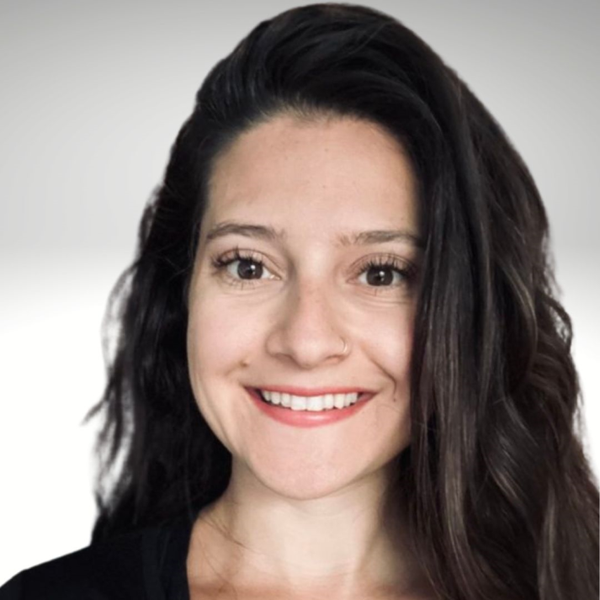 A smiling person with long, dark, wavy hair, centered against a soft, light gray gradient background.