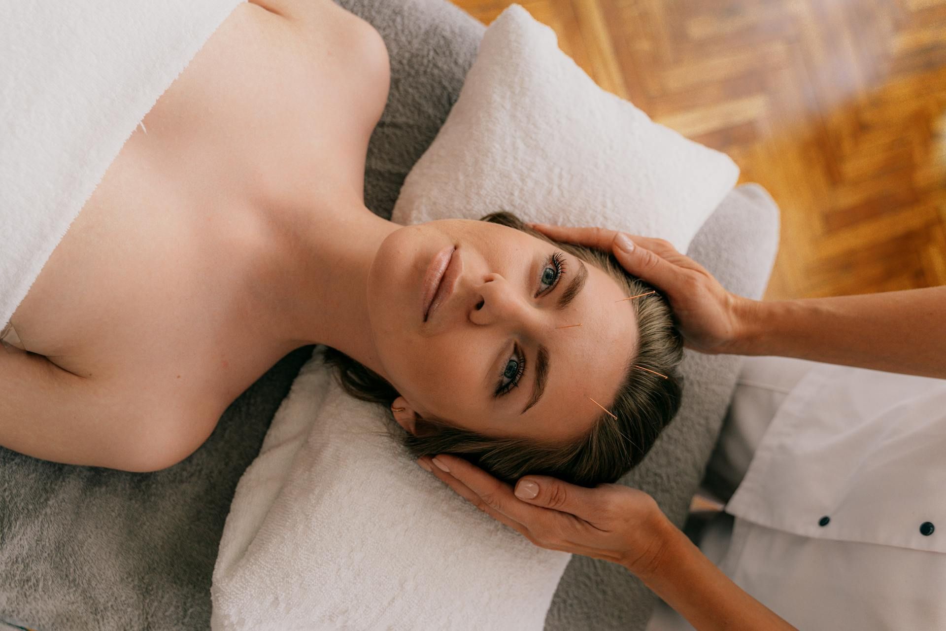 A person lying on a massage table receiving a head massage from a practitioner.