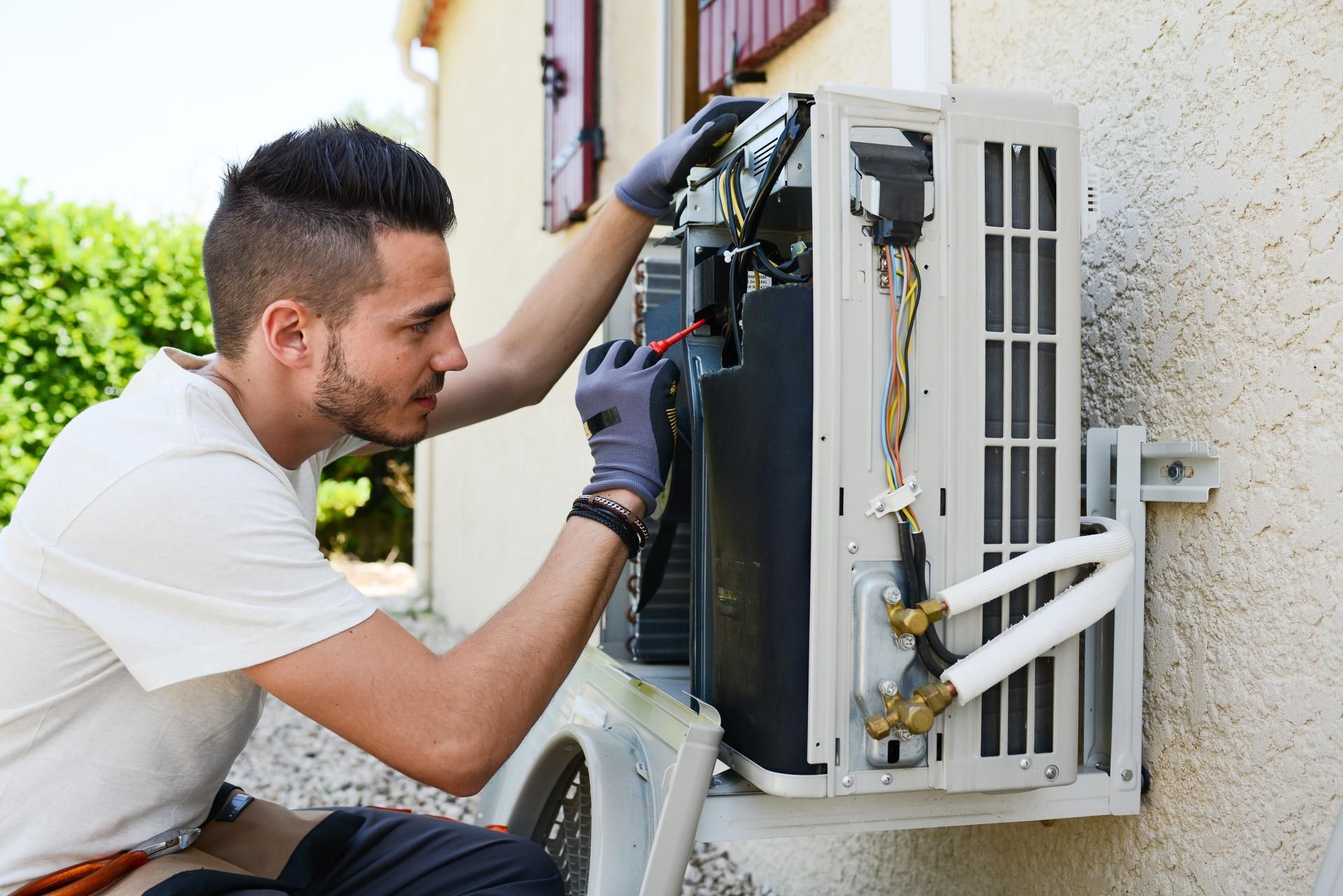 A man is working on an air conditioner outside of a house.