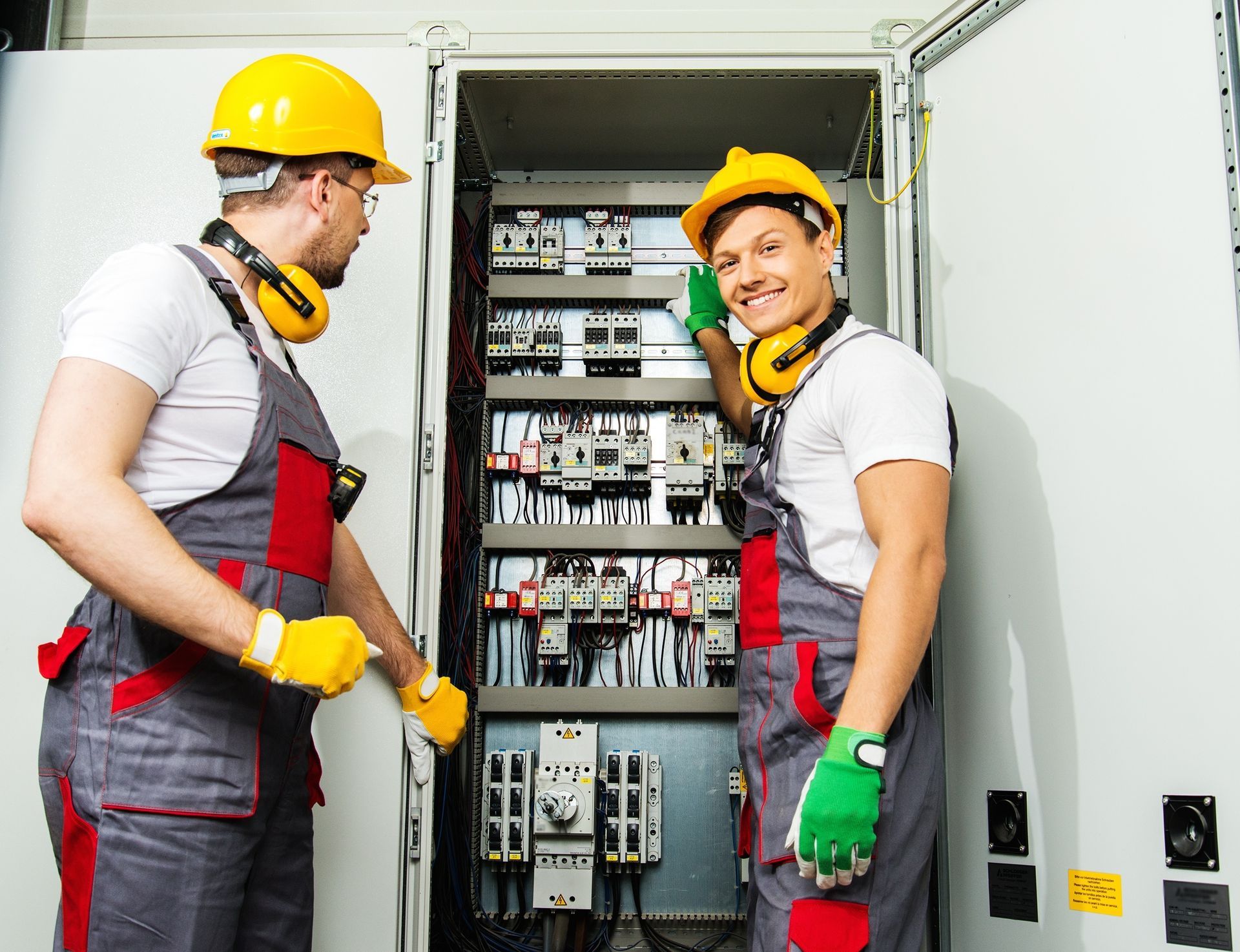 Two electricians in a safety hat and headphones on a factory.
